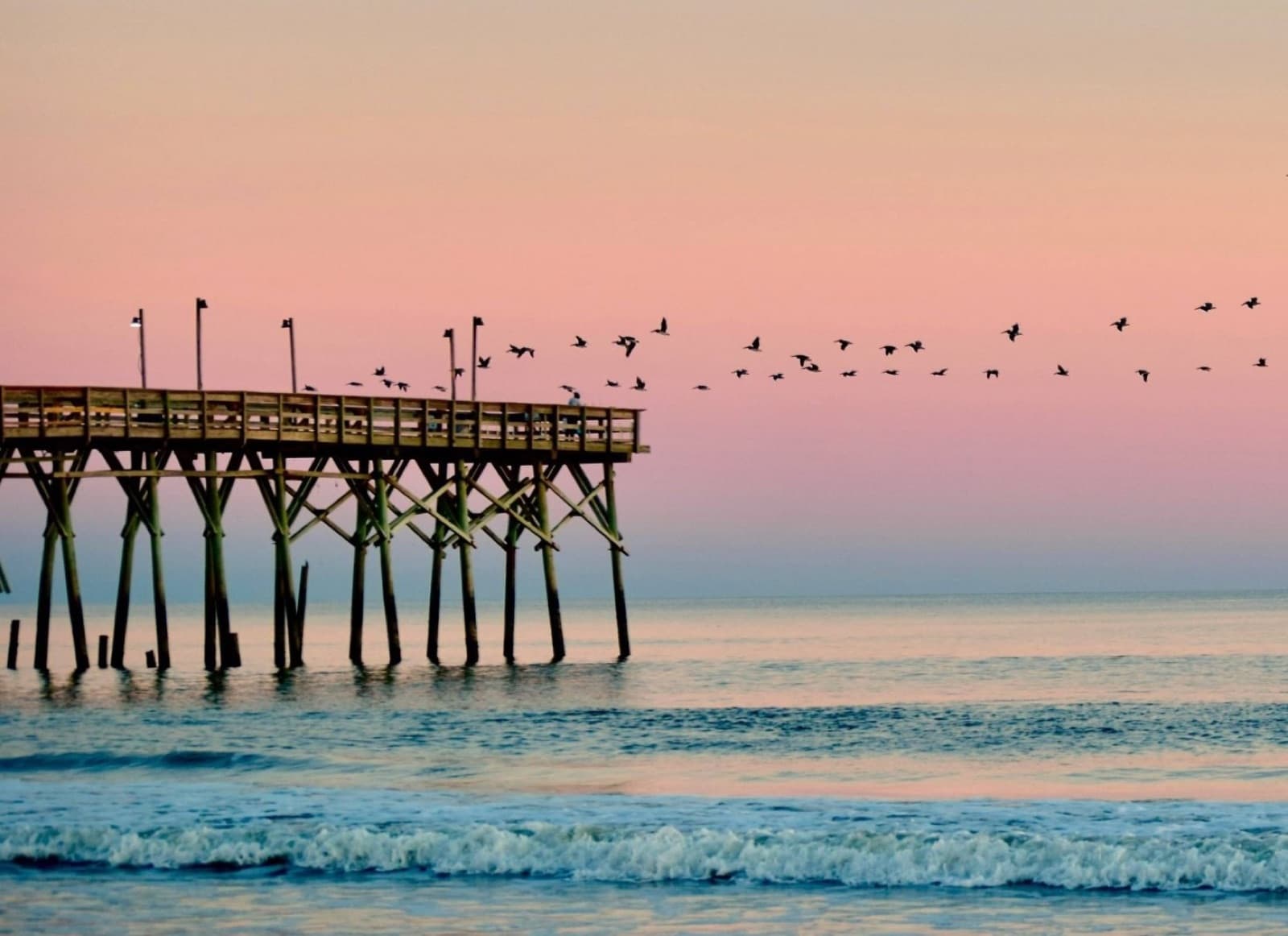 OIB Pier at sunset with a flock of birds skimming overhead