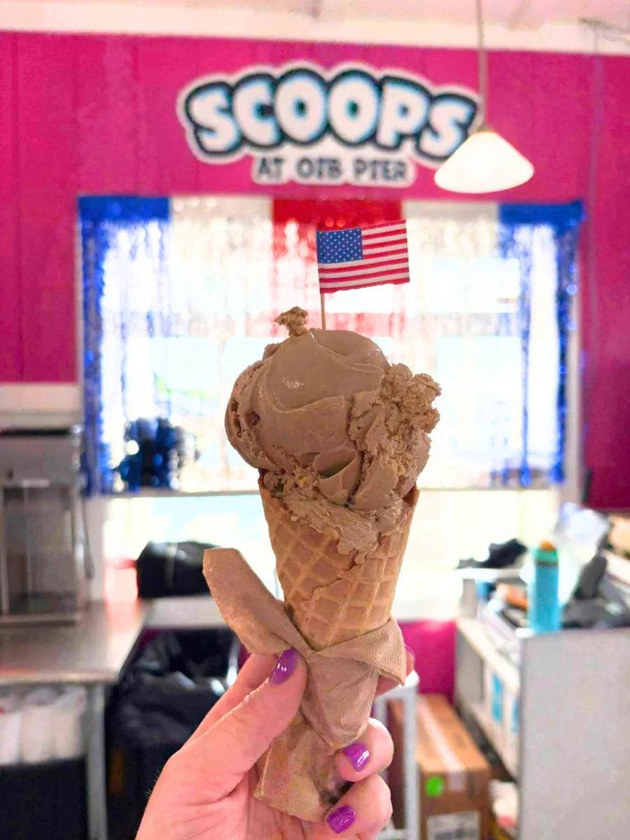 A chocolate scoop cone in front of the Scoops sign