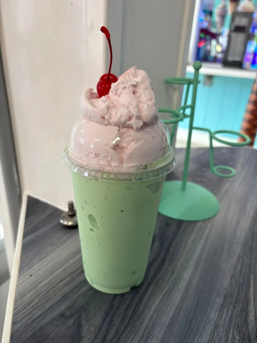 A mint green milkshake topped with whipped cream and a cherry