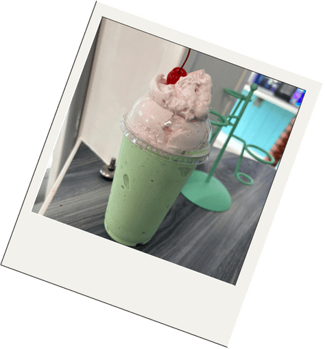 A mint green milkshake topped with whipped cream and a cherry
